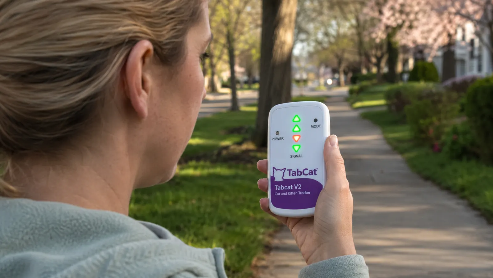 Person holding a small white Tabcat handheld receiver outdoors, screen showing directional arrows and signal bars
